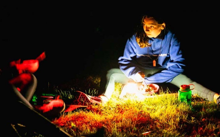 a girl illuminated by a lamp eats while on an outward bound course 